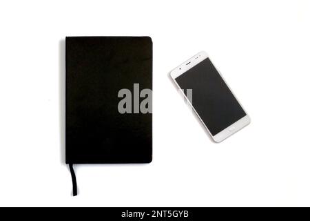 A black leather notebook by the side of a white unmarked smartphone on a white background. Stock Photo