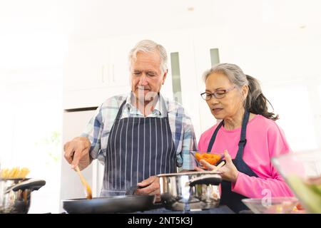 Happy senior diverse couple cooking dinner in kitchen Stock Photo