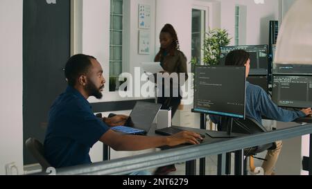 African american developer using laptop to write code and display system information on computer. Database coder parsing algorithm working on user interface in software agency. Stock Photo