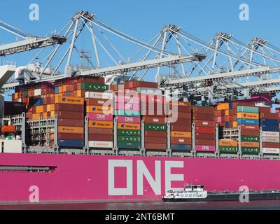 Large pink container ship from the Japanese ONE Ocean Network Express with small fuel ship next to it in the Port of Rotterdam, the Netherlands Stock Photo