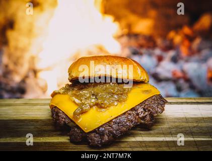 Smashed Cheeseburger on a wooden table in front of a fireplace. Stock Photo