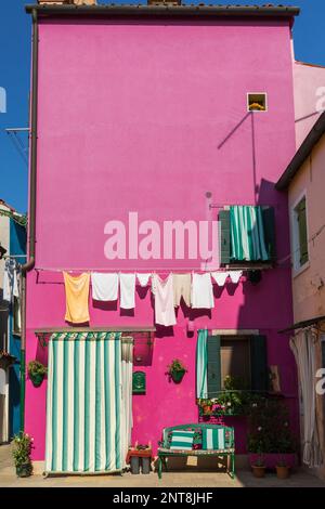 Clothesline on wall of pink stucco house decorated with green and white striped curtains over entrance door and window, Burano Island, Italy. Stock Photo