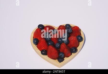 Strawberries and blueberries in a heart shaped wooden container placed on a white background. Stock Photo