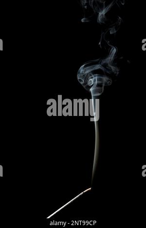 Burning incense stick and its smoke on a black background. Stock Photo