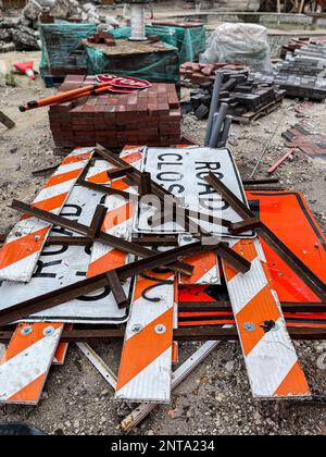 Road closed signs sit stacked among bricks and other supplies at road construction site. Stock Photo