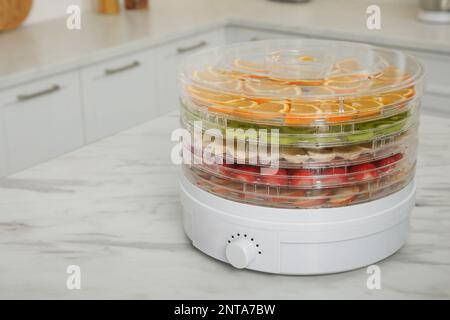 Dehydrator machine with different fruits and berries on white marble table in kitchen, space for text Stock Photo