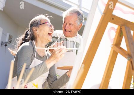 Happy senior diverse couple painting on easel in garden Stock Photo