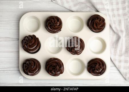 Delicious chocolate cupcakes with cream in baking tray on white wooden table, top view Stock Photo