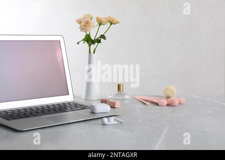 Modern laptop, flowers and makeup products on grey marble table. Space for design Stock Photo