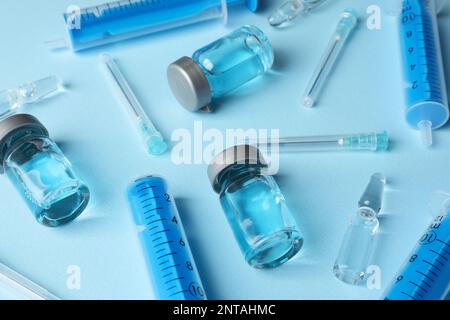 Disposable syringes with needles, ampules and vials on light blue background Stock Photo