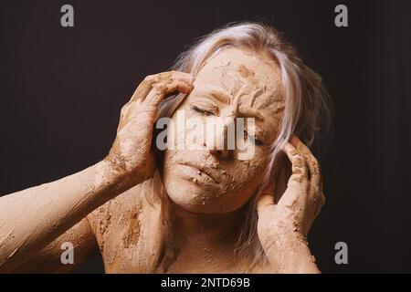 woman covered in dry cracked clay mud mask holding her head in pain Stock Photo
