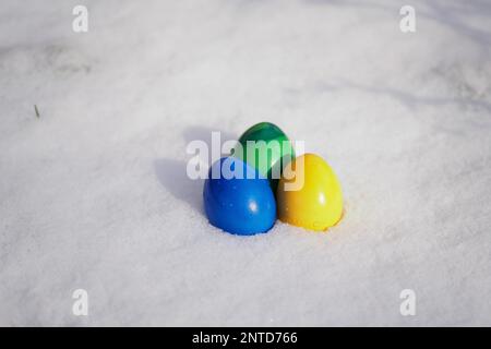 three easter eggs painted in vibrant colors laying in fresh snow Stock Photo