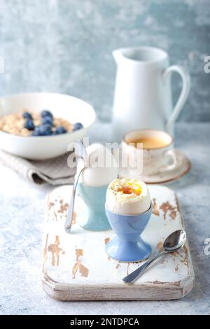 Fresh soft boiled eggs, oatmeal with blueberries, coffee cup, milk jug. White concrete rustic background. Soft eggs, healthy breakfast. Selective Stock Photo