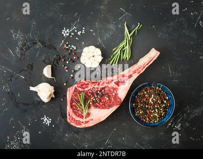Raw marbled meat steak, herbs, seasonings, garlic, rustic stone background. Beef Rib eye steak on bone, ready for cooking. Top view. Ingredients for Stock Photo