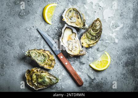 Fresh oysters on ice, knife, lemon wedges. Rustic stone background. Opened fresh raw oysters. Top view. Close-up. Oyster bar. Seafood. Oysters Stock Photo