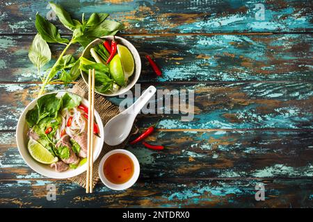 Traditional Vietnamese soup Pho bo with herbs, meat, rice noodles, broth. Pho bo in bowl with chopsticks, spoon. Space for text. Top view. Asian soup Stock Photo