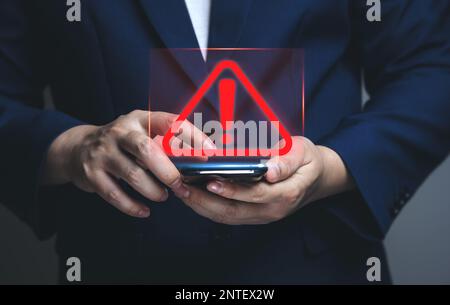 Businessman using smartphone with warning triangle showing a system error. Concepts of system maintenance, security, anti-virus Stock Photo