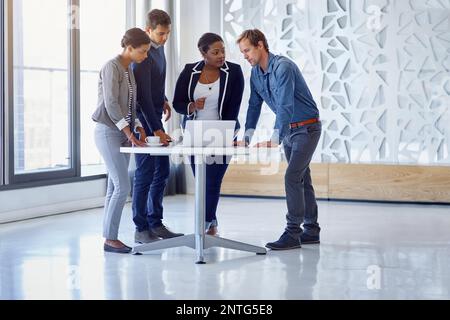 Putting their heads together for success. a group of coworkers working together on a laptop in an office. Stock Photo