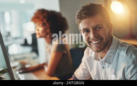 I get more done at night. a young designer working late with his colleague blurred in the background. Stock Photo