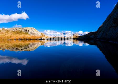 The main range of Brenta Dolomites, partially shrouded in clouds, reflected in a small lake near Lago Nero. Stock Photo