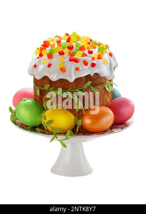 Easter Сake with white sugar icing, decorated with dried candied fruits and Easter eggs. Easter food on cakestand isolated on white background. Stock Photo