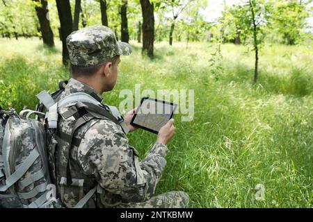 Soldier with backpack using tablet in forest Stock Photo