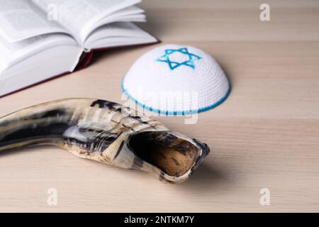 Shofar and Kippah with Star of David near open Torah book on wooden table. Rosh Hashanah holiday attributes Stock Photo