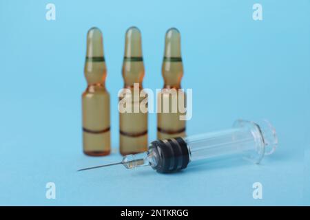 Disposable syringe with needle and ampules on light blue background Stock Photo