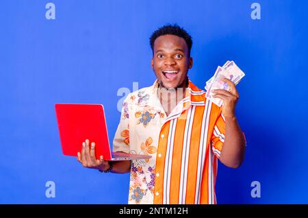 Photo of a happy young afro american handsome man posing isolated over blue wall background using laptop computer holding money. Stock Photo
