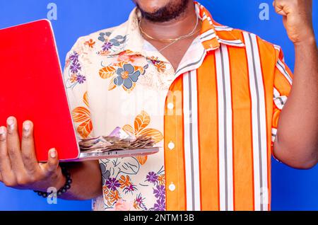 Photo of a happy young afro american handsome man posing isolated over blue wall background using laptop computer holding money. Stock Photo