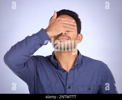 Hand, face and regret with a man in studio on a gray background feeling disappointed by a mistake. Facepalm, problem and frustrated with a male Stock Photo