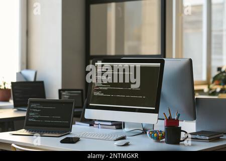 Modern workplace of developer with computers with programming codes on screens in IT office Stock Photo