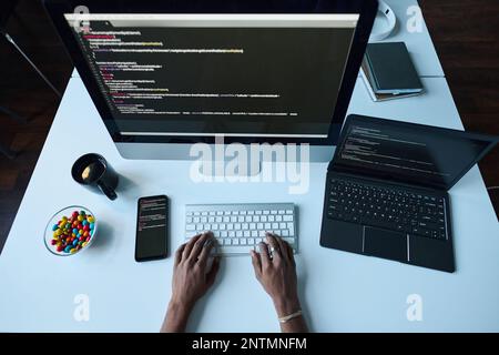 High angle view of developer sitting at table in front of computer monitor and typing security codes for software Stock Photo