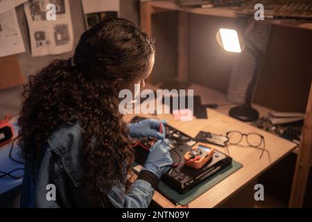 Computer retro repair shop. Female engineer performing laptop maintenance. Hardware developer fixing electronic components, voltage measurement with m Stock Photo