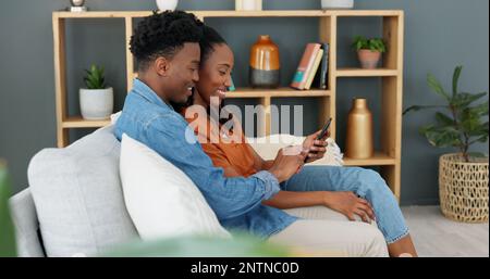 Internet, technology and couple with phone on sofa in living room. Black man teaching young woman how to use banking app, online shopping or fintech Stock Photo