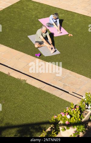 Happy senior diverse couple doing yoga and stretching in garden Stock Photo