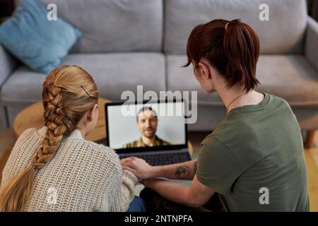Back view of wife and daughter watching video message from father serving in military Stock Photo