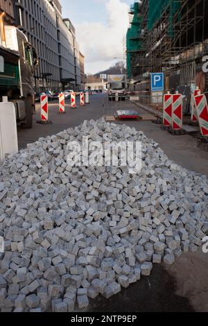 A building under construction on the right, the street is under construction, in the foreground small square cobblestones are piled up. Stock Photo