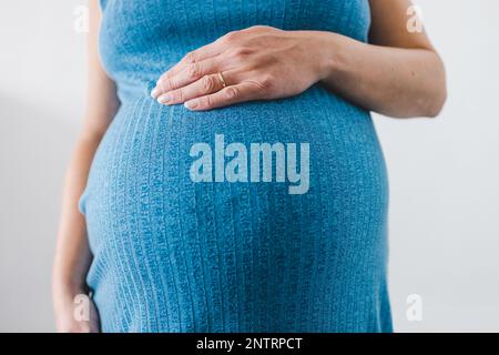 pregnant woman cudling her bump in the ninth month, mid-section showing the belly and body shape wearing blue dress Stock Photo