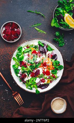 Beet, cheese and orange healthy salad with arugula, lamb lettuce, red onion, walnut and tangerine, brown kitchen table. Fresh useful dish for healthy Stock Photo