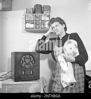 Radio listeners in the past. A woman in the kitchen has stopped what she is doing there and is seen standing listening to something important or a nice tune from the radio. On the front of the radio is a scale and when you turned the dial next to it so that the pointer was in the middle of a station name, that station was there. In addition to FM broadcasts, they also listened to foreign radio on longwave. Sweden in 1945 Kristofferson ref M4-3 Stock Photo