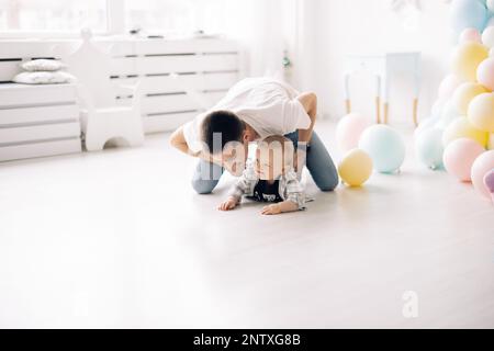 Happy father plays with his son celebrating first birthday of baby boy among a lot of colorful balloons. Celebration first birthday. Festive event. Stock Photo