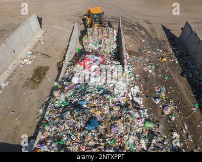 Skid steer loader moving plastic garbage with scrap grapple on the landfill site, drone shot. Waste disposal concept. Stock Photo