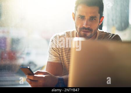 Getting some admin done. Shot of a young man using his laptop in a coffee shop. Stock Photo