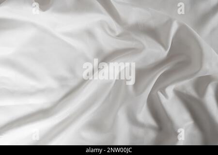 Satin crumpled fabric of white color, top view. Natural bed linen, sheets, abstract background of luxury fabric, wavy folds Stock Photo