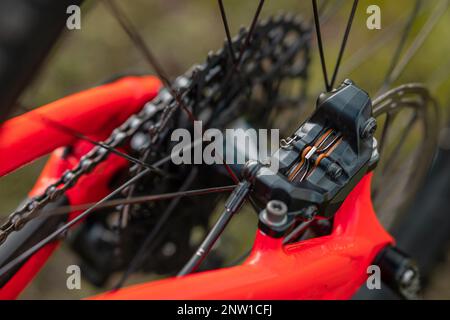 View of a rear brake on a modern mountain bicycle. Visible caliper with four pistons and fresh brake pads with orange backing. Brake pad service. Stock Photo
