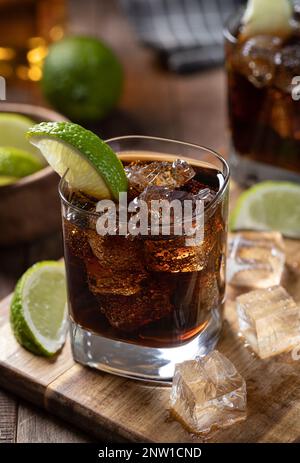 Rum and cola cocktail with sliced lime and ice on a wooden board Stock Photo