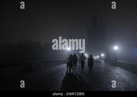 A group of young people is walking on the charles bridge in prague during night time. Scary spooky moment on a hazy and misty bridge. Stock Photo