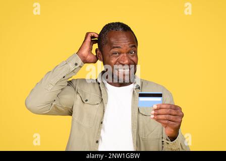 Confused mature black male in casual scratching head, thinking, show credit card Stock Photo