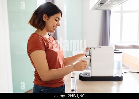 Beautiful Young Arab Woman Using Modern Coffee Machine In Kitchen Stock Photo